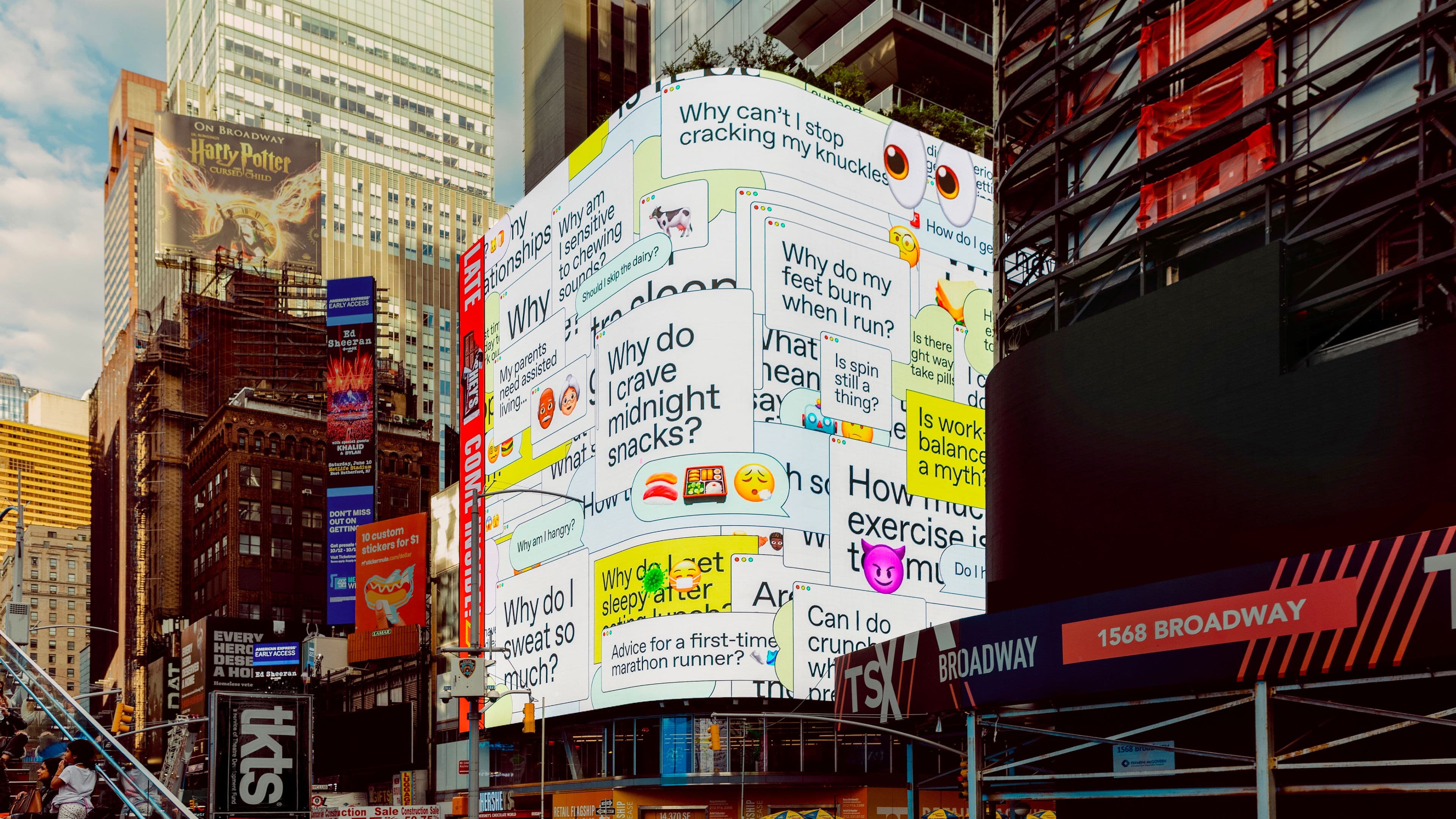 A large electronic billboard in Times Square displays colorful, overlapping health-related questions with emojis.